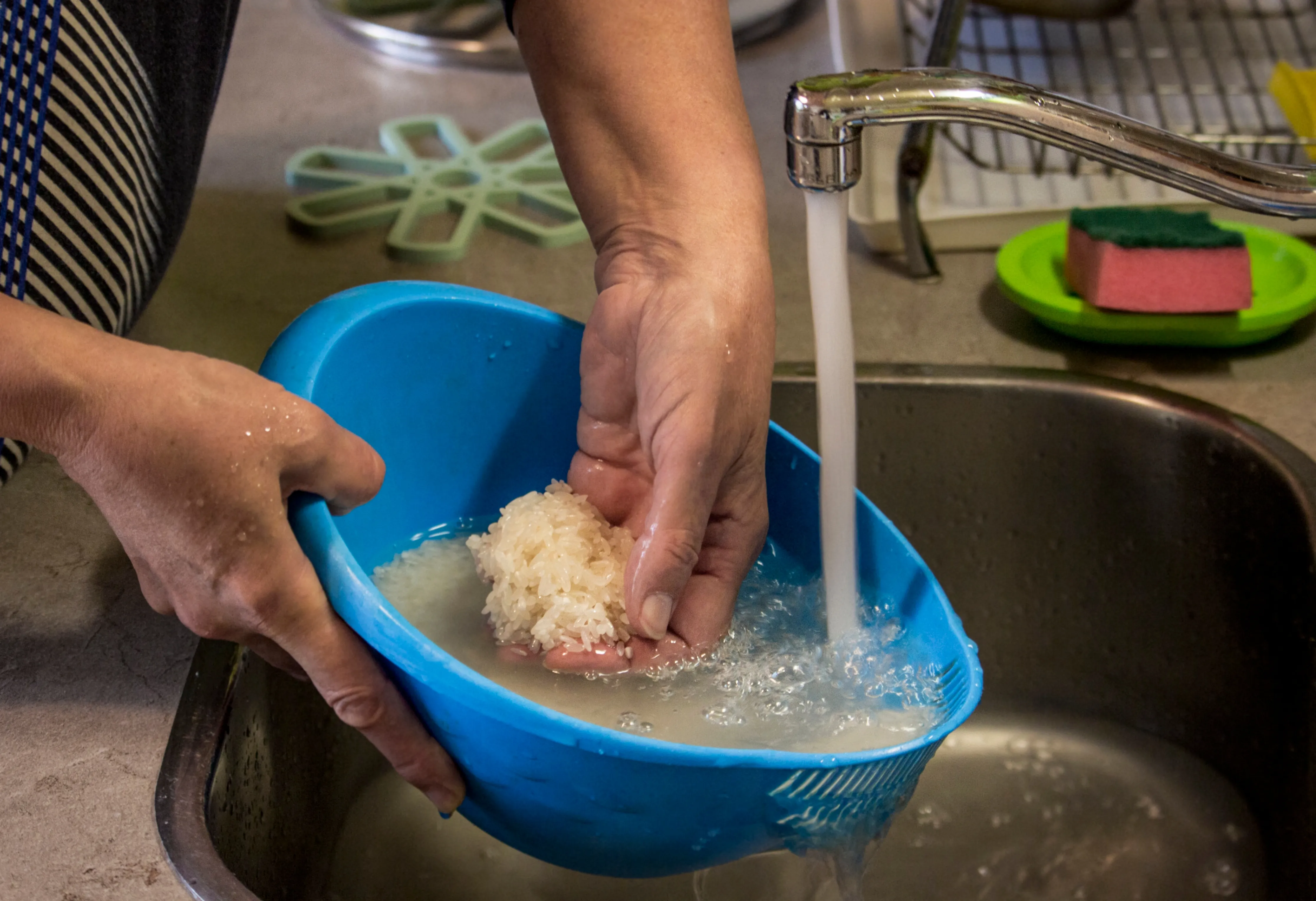 null Woman washes raw rice at the kitchen tap.