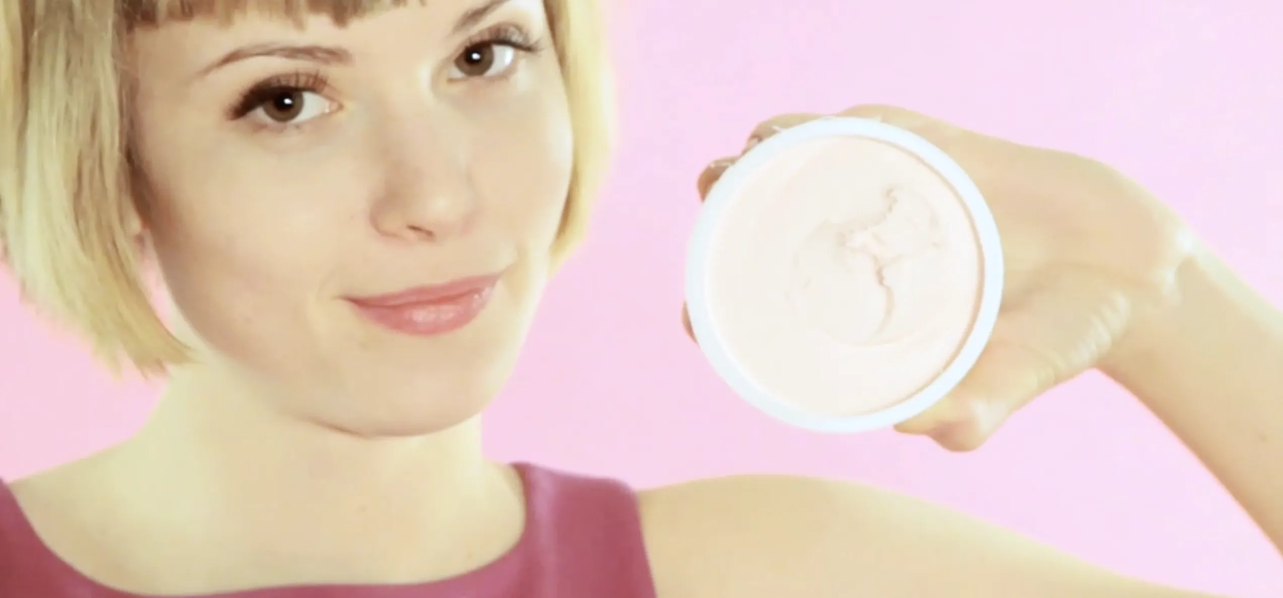 Woman showcasing an open can of frosting/icing against a pink background.