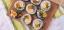 Colorful sushi rolls arranged on a wooden plate on top of a striped green and yellow tea towel.