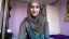 Young woman wearing a hijab, smiling in a modest indoor setting.