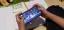 Person playing a mobile game while studying with an open notebook and pencil nearby.