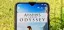 Assassin's Creed Odyssey displayed on a smartphone screen outdoors.