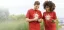 Two people in red shirts looking at their smartphones while walking outdoors.