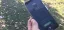 A hand holding a smartphone displaying a call interface outdoors on grass.
