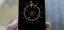 A hand holds a smartphone displaying a digital compass app, showing a heading of 55 degrees northeast. The background is blurred with neutral tones.