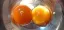 A close-up photo of two raw egg yolks in a silver bowl, one a dark orange, one a bright yellow.